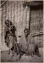 Two men in front of a thatched structure