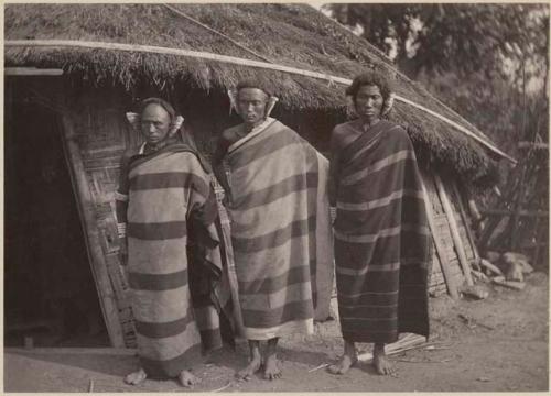 Three men standing in front of a thatched structure