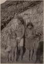 Women and children in front of a thatched structure