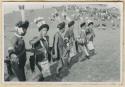 Men in line, crowd on hillside in background