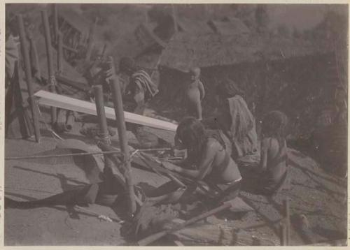 Women working on looms surrounded by children