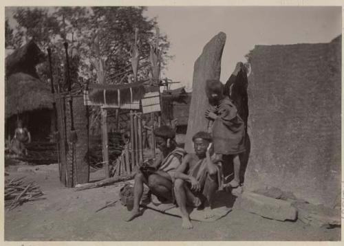 Men sit between decorated bamboo structure and stone tablets