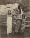 Three girls and boy in front of boat with thatch roof