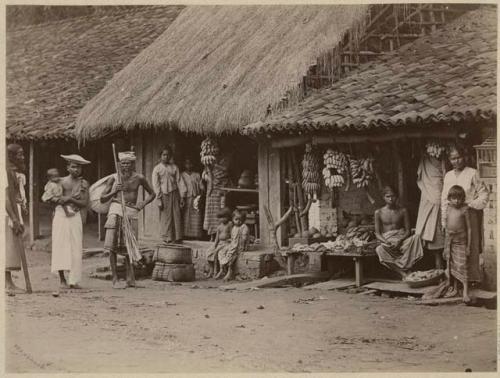 People in front of building, with bananas hanging from roof