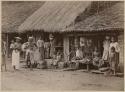 People in front of building, with bananas hanging from roof