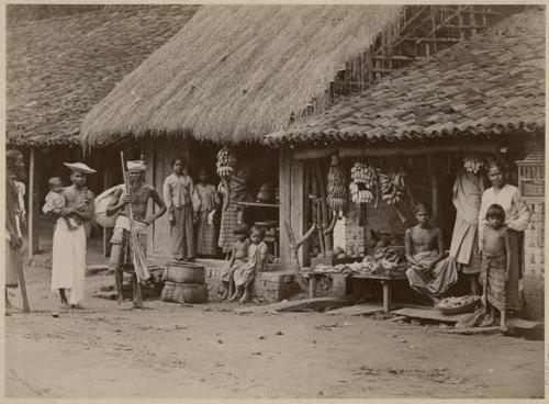 People in front of building, with bananas hanging from roof