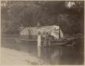 Group surrounding boat with thatched roof in water