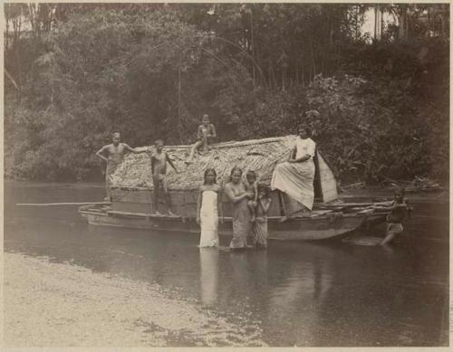 Group surrounding boat with thatched roof in water