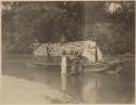 Group surrounding boat with thatched roof in water