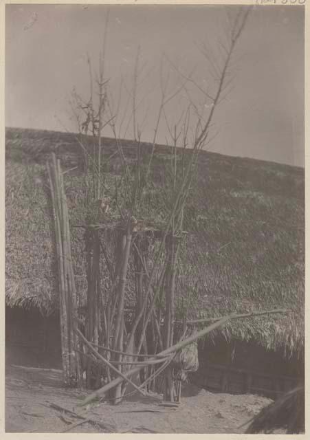 Small bamboo structure in front of building with thatched roof