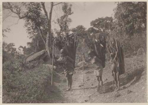 Women and boy carrying wood in baskets on their back