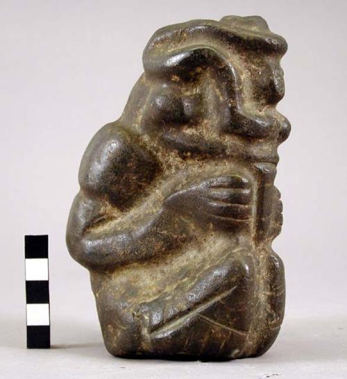 Black stone figure, depicting a man blowing or sucking on a tube