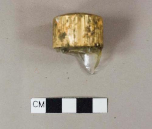 Colorless glass bottle external threaded finish, inside plastic screw cap covered in thin gold-colored metal, embossed with an unidentifiable design on top of cap