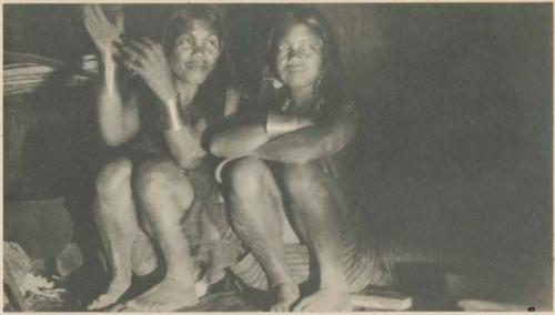 Two women cooking rice, sitting on blocks of wood near the fire