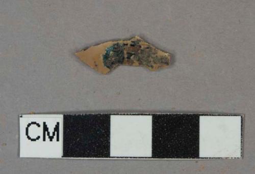 Tan flat plastic fragment, remainder of label on one side