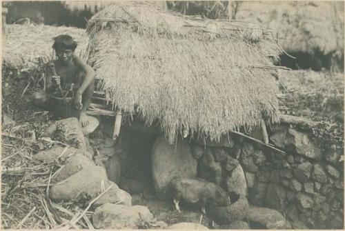 Igorot boy sitting next to pig pen with stone troughs