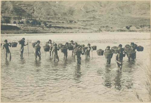 Igorot men carrying baskets of manure across river