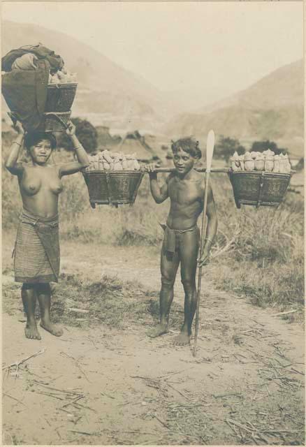 Igorot man and woman walking with baskets of camotes