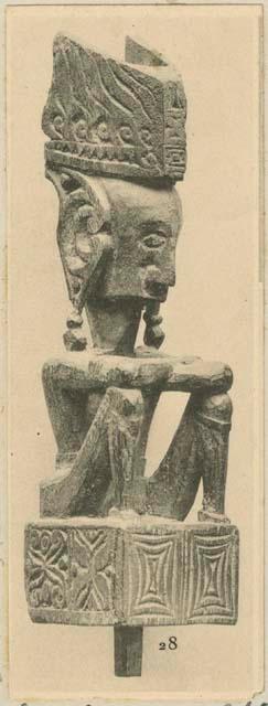 Wood sculpture of a divinity seated on a cubic pedestal, with arms crossed, legs folded and elbows on knees