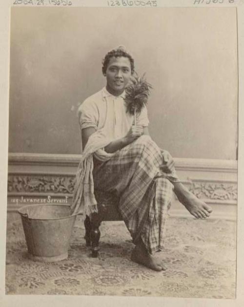 Studio portrait of male servant sitting and holding feather duster