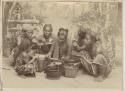 Men, woman, and children eating staged meal in front of painted backdrop