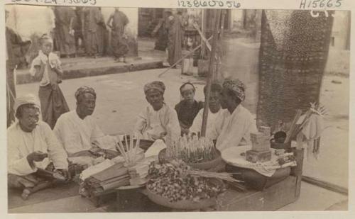 Men sit around outdoor table with street in background