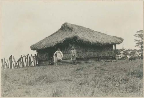 Two Benguet Igorot people standing in front of a grass house