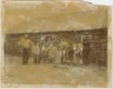 Group of people and children standing outside stone house with thatched roof