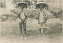 Two Ilocano men using palm leaves as rain shield