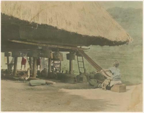 Igorot woman working loom underneath house