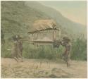 Men carrying small house, mountain landscape in background