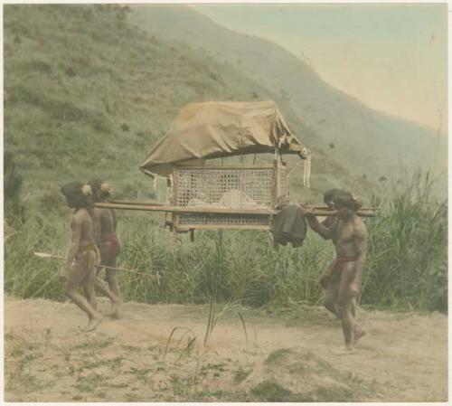 Men carrying small house, mountain landscape in background