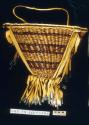 Twined burden basket with leather fringe and tin tinkers