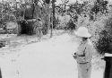Expedition member watching a woman wearing a dress walk toward an enclosure in the camp, view from behind