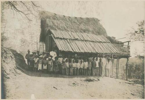 Students standing with teacher in front of schoolhouse