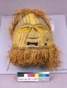 Carved wood mask with yellow painted decorations; leather and raffia trim