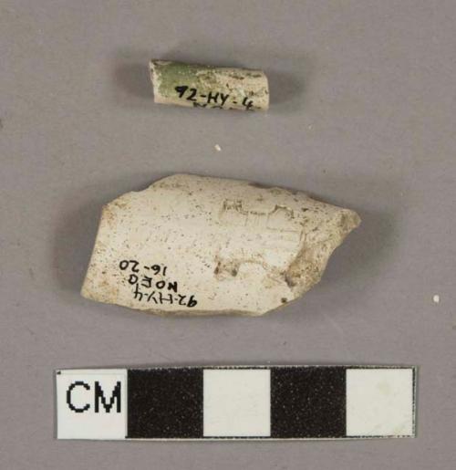 White kaolin pipe fragments, 1 pipe bowl with stamped cred of shield with cross, 1 pipe stem fragment with green, painted mouthpiece and 5/64" bore diameter.