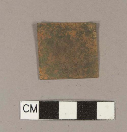 Square copper alloy sheet fragment with some flecks of silver metallic material on the surface