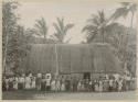 Group of adults and children in front of thatched structure