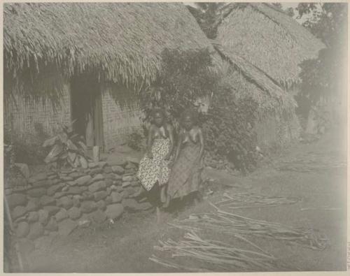 Two women in front of thatched houses