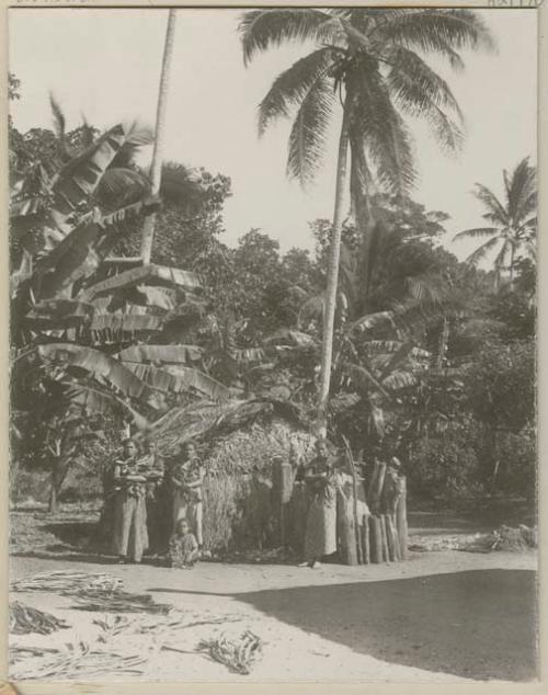 Women and children in front of small thatched structure