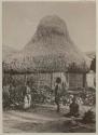 Man and two women and in front of thatched structure with rounded roof peak