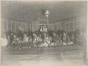 Women sitting on a mat, dancing, with onlookers including Western sailors in the doorway