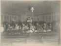 Women sitting on a mat, dancing, with onlookers including Western sailors in the doorway