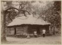 Two people in front of thatched house