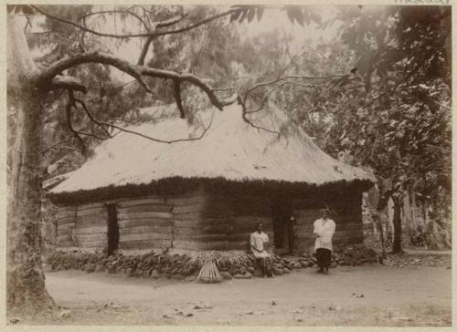 Two people in front of thatched house