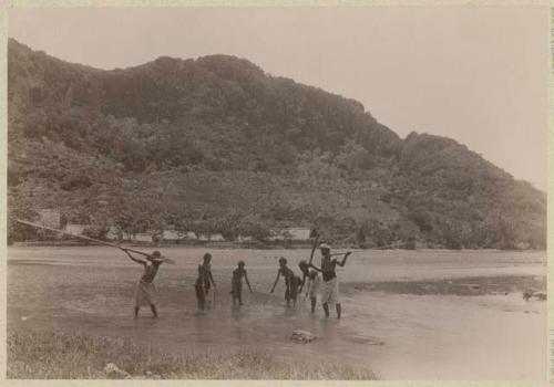 Fishers standing in the water with nets and spears