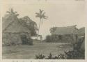 Person standing between two thatched buildings