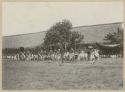 Group of people with clubs standing, others seated watching, possibly part of wedding ceremony