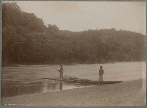 One man in canoe on Rewa River, one man standing on shore with oar